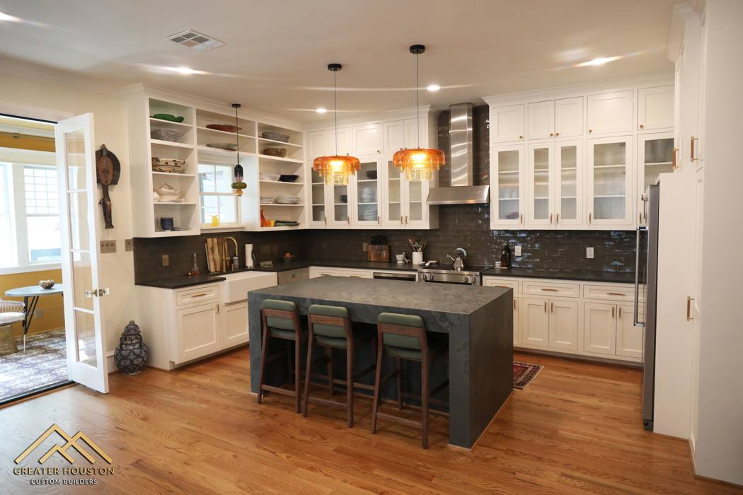 Renovated kitchen with white cabinetry, a dark stone island, and wood floors, completed by Greater Houston Custom Builders